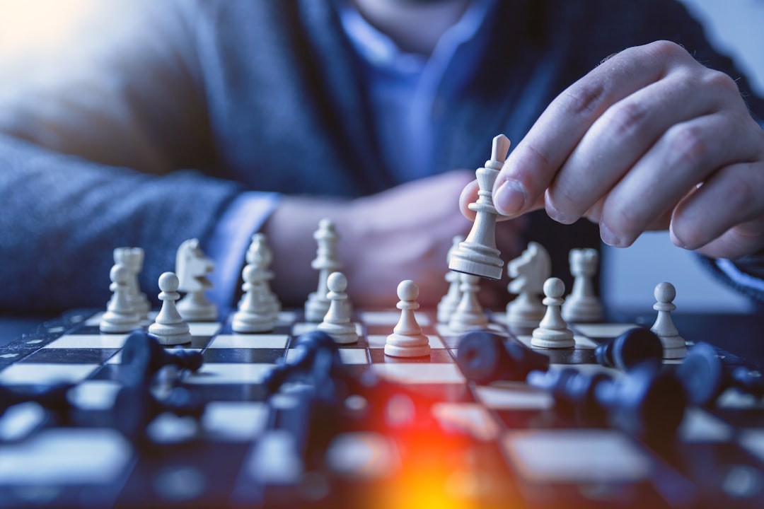 Person in a suit playing chess, moving a white king piece on a chessboard.